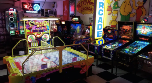 A vibrant arcade filled with retro games, including air hockey, pinball machines, and colorful neon signs.