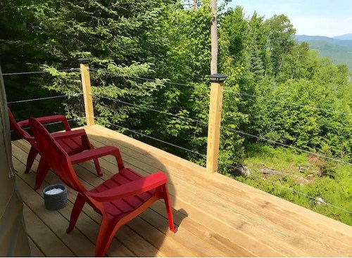 Two red chairs on a wooden deck overlooking a lush green forest and distant mountains.