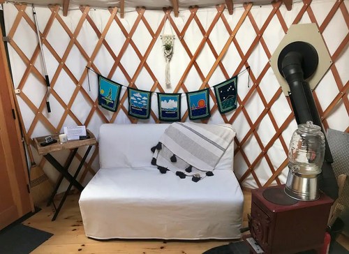 Cozy interior of a yurt featuring a white couch, decorative banners, a wood stove, and rustic decor.