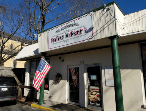 Exterior of an Italian bakery with a sign, American flag, and clear blue sky.