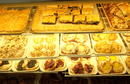 A display case filled with various pastries, including baklava, fruit tarts, and cinnamon rolls.