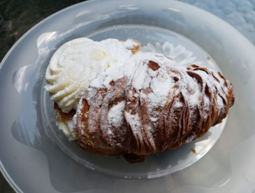 A flaky pastry topped with powdered sugar and cream, served on a clear glass plate.