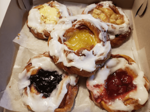A box of five sweet pastries with various fruit fillings and white icing on top.