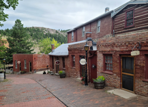 A charming brick building with a cobblestone path, surrounded by greenery and mountains in the background.