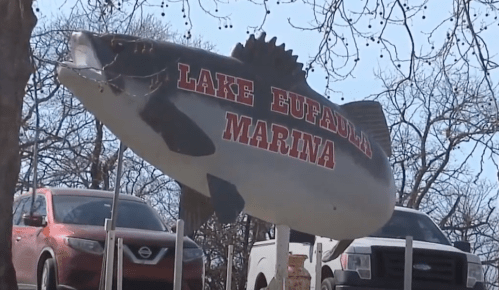 A large fish sign reading "Lake Eufaula Marina" with trees and parked cars in the background.