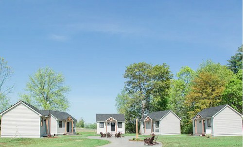 A cluster of small, white cottages surrounded by green trees and a clear blue sky.