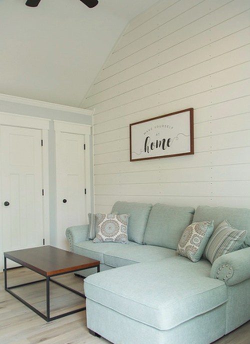 Cozy living room with a light blue sectional sofa, decorative pillows, and a wooden coffee table against a shiplap wall.