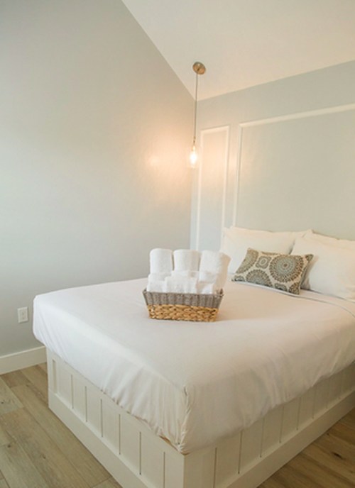 A cozy bedroom featuring a white bed with decorative pillows and a basket of rolled towels on the bed.