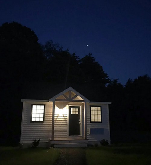 A small, illuminated house at night, surrounded by trees, with a bright star visible in the sky above.