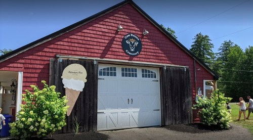A red barn with a sign for ice cream, featuring a large ice cream cone decoration and lush greenery outside.