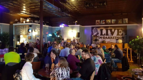 A lively crowd enjoying an event in a cozy venue with a stage and colorful decor.