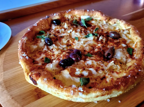 A freshly baked pizza topped with cheese, olives, and herbs on a wooden board.