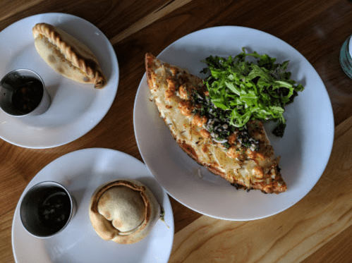 A plate with a large cheesy dish, a side salad, and two smaller pastries on the side.