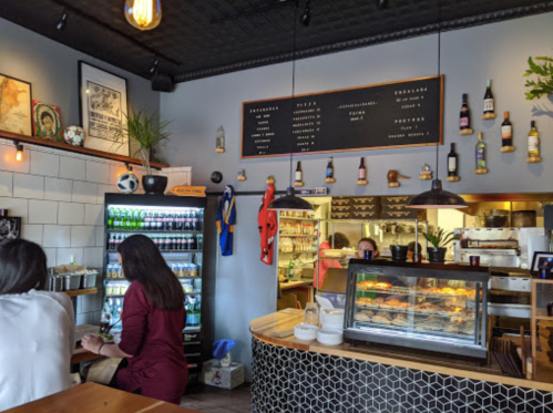 Cozy café interior with a counter, menu board, drinks fridge, and decor including plants and sports jerseys.