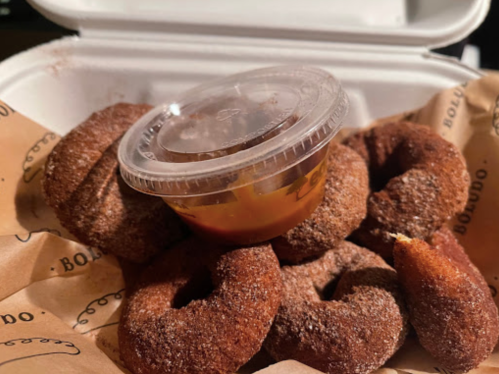 A takeout container filled with cinnamon sugar donuts and a small cup of dipping sauce on top.