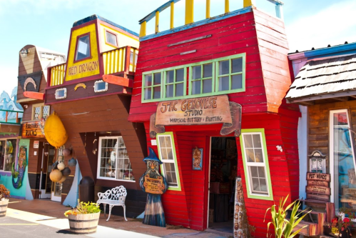 Colorful, whimsical storefronts with unique architecture, featuring a sign for "The Genwee Studio" and vibrant decorations.