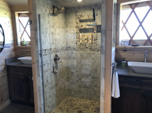 A modern shower with stone tiles, glass enclosure, and wooden accents in a well-lit bathroom.