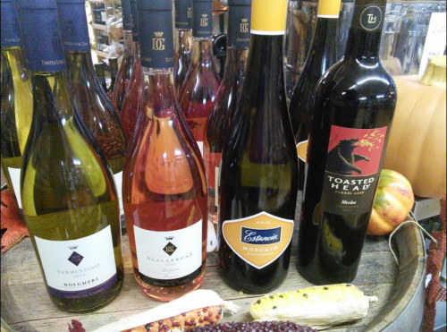 A selection of wine bottles, including white, rosé, and red varieties, displayed on a wooden barrel with autumn decor.