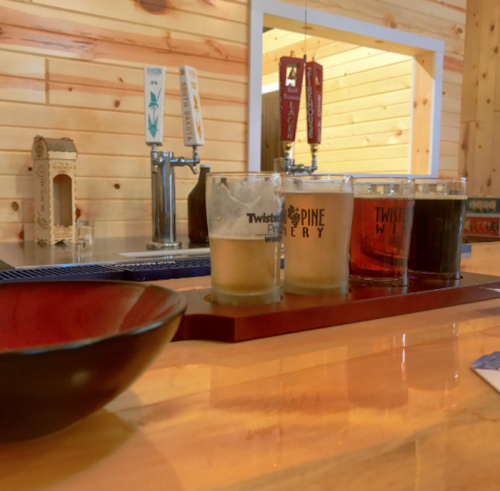 A wooden bar with a flight of four beer glasses and a bowl, set against a rustic wooden backdrop.