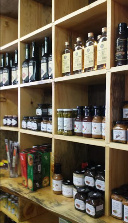 Shelves filled with various bottles and jars of sauces, oils, and spices in a rustic wooden display.
