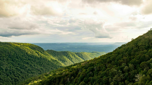 Lush green mountains stretch under a cloudy sky, showcasing a serene valley landscape.