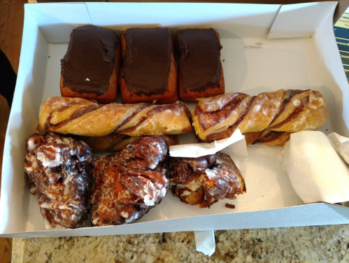 A box of assorted pastries, including chocolate-covered donuts, cinnamon rolls, and glazed pastries.