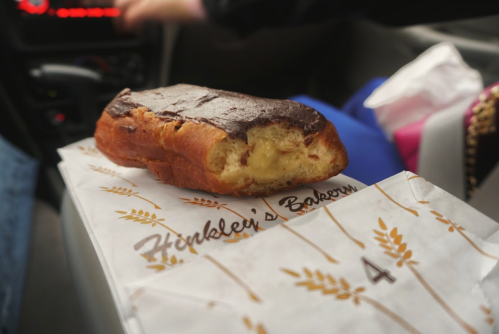 A partially eaten pastry with chocolate frosting on a paper from Henklee's Bakery, resting in a car.