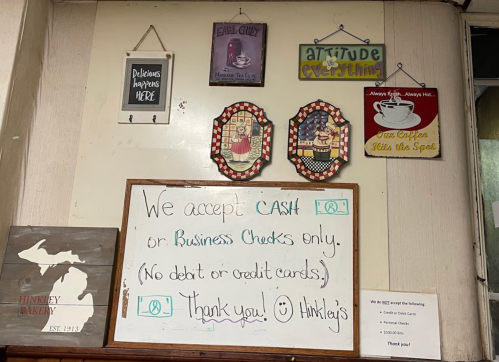A wall display with signs about payment methods, including a large whiteboard stating "We accept CASH or Business Checks only."