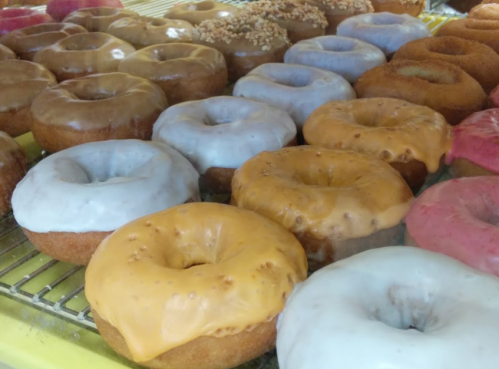 A variety of donuts in different colors and glazes, arranged on a display rack.
