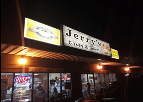 Sign for "Jerry's Cakes & Donuts" illuminated at night, with a view of the shop's windows and an "OPEN" sign.