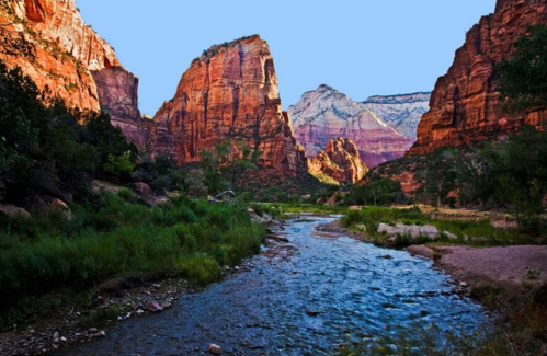 A scenic view of red rock formations and a winding river surrounded by lush greenery in a canyon.