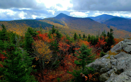A scenic view of mountains and vibrant autumn foliage under a partly cloudy sky.