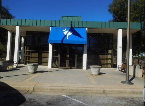 A modern building with a blue awning featuring a palm tree logo, surrounded by benches and planters.