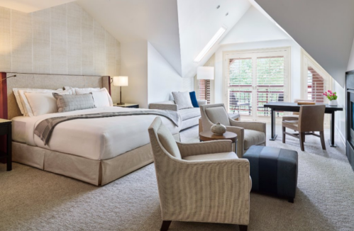 A spacious, modern hotel room with a king bed, seating area, desk, and large windows overlooking a balcony.
