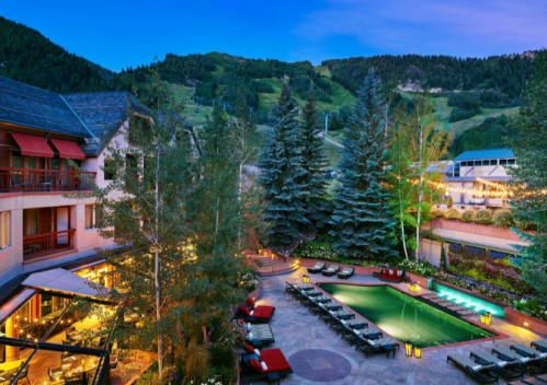 A scenic view of a hotel pool surrounded by trees and mountains at dusk, with lounge chairs and soft lighting.