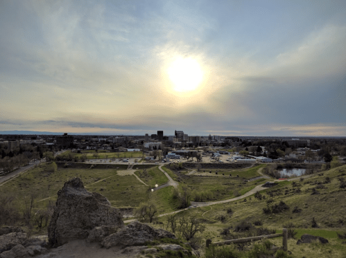 A scenic view of a city skyline at sunset, with green hills and a winding path in the foreground.