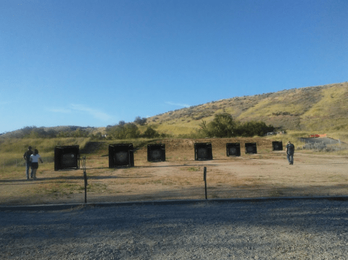 A shooting range with several target frames set against a hilly landscape under a clear blue sky.