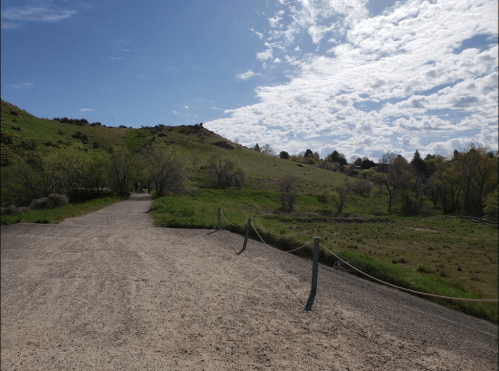 A gravel path leads through a green landscape under a partly cloudy sky with scattered trees and hills in the background.