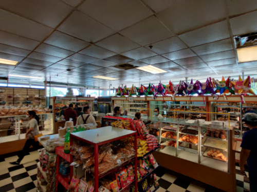 A colorful grocery store interior with shelves of snacks, baked goods, and festive decorations. Customers browse the aisles.
