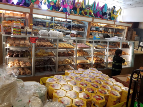 A bakery display filled with various pastries and bread, with a child reaching for treats in the foreground.