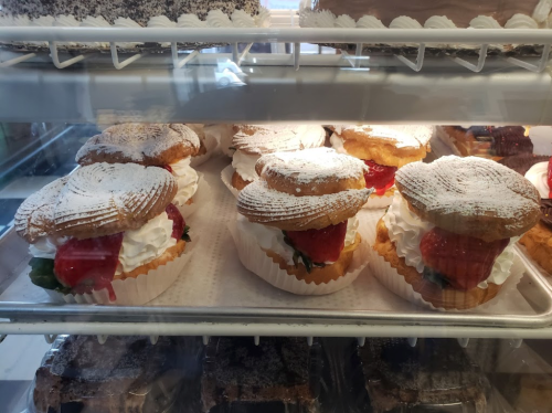Delicious strawberry shortcakes with whipped cream, dusted with powdered sugar, displayed in a glass case.