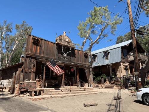 A rustic building with an American flag, surrounded by trees and power lines, under a clear blue sky.