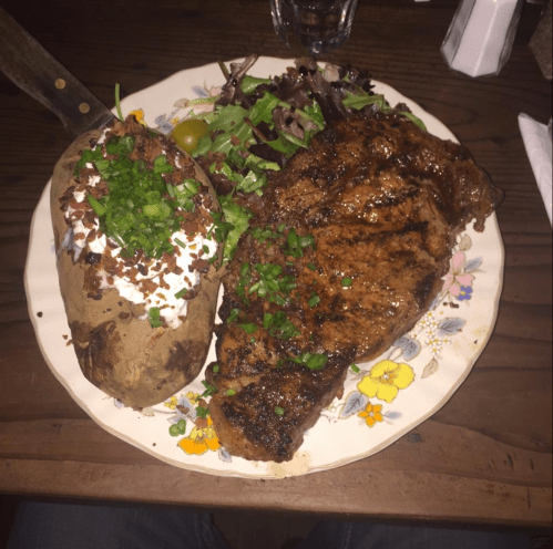 A plate featuring a grilled steak, a loaded baked potato with toppings, and a side salad.