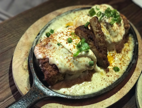 Sizzling skillet with meatloaf topped with creamy sauce and green onions, served on a wooden board.