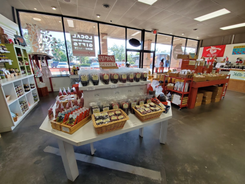 A bright store interior featuring shelves of local products, including jars, snacks, and a display of cherries on a table.