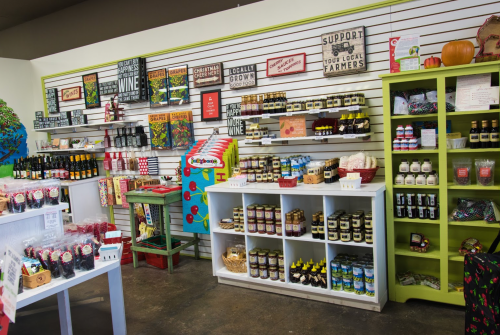 A vibrant store display featuring local products, jars, and signs promoting local farmers and seasonal items.