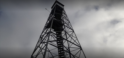 A tall metal tower against a cloudy sky, featuring a staircase and a small platform at the top.