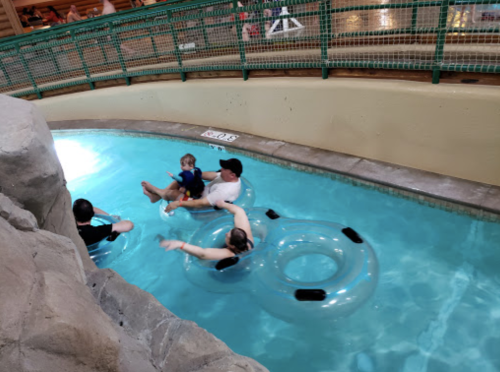 A family enjoys a water slide in a pool, floating on inner tubes and relaxing together.