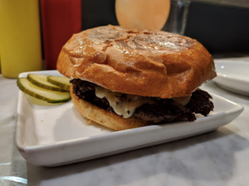 A juicy burger with melted cheese on a toasted bun, served with pickles on a white plate.