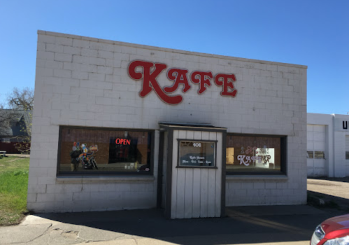 A small café building with a sign reading "KAFE" and an "OPEN" sign in the window on a sunny day.